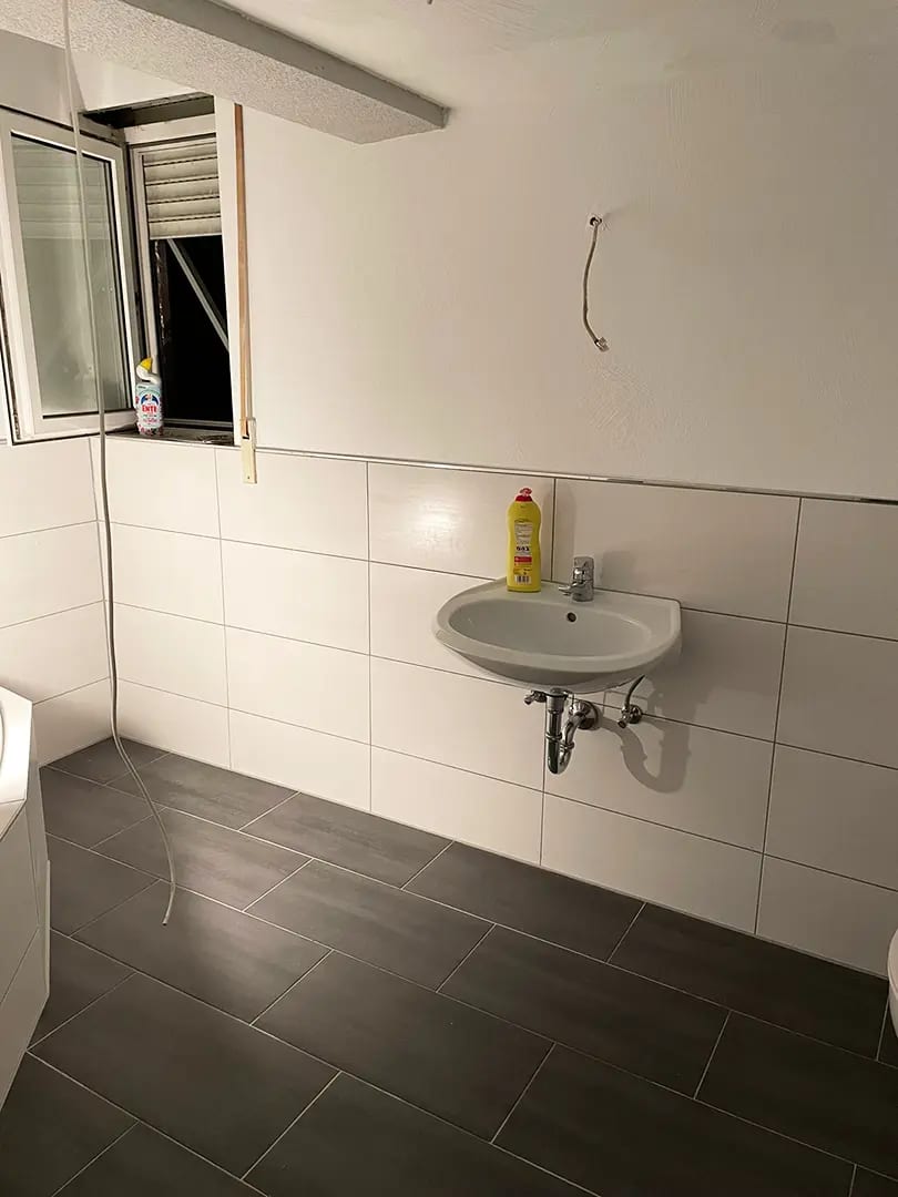 Bad mit neuen weißen Wandfliesen, dunklen Bodenfliesen und montiertem Waschbecken