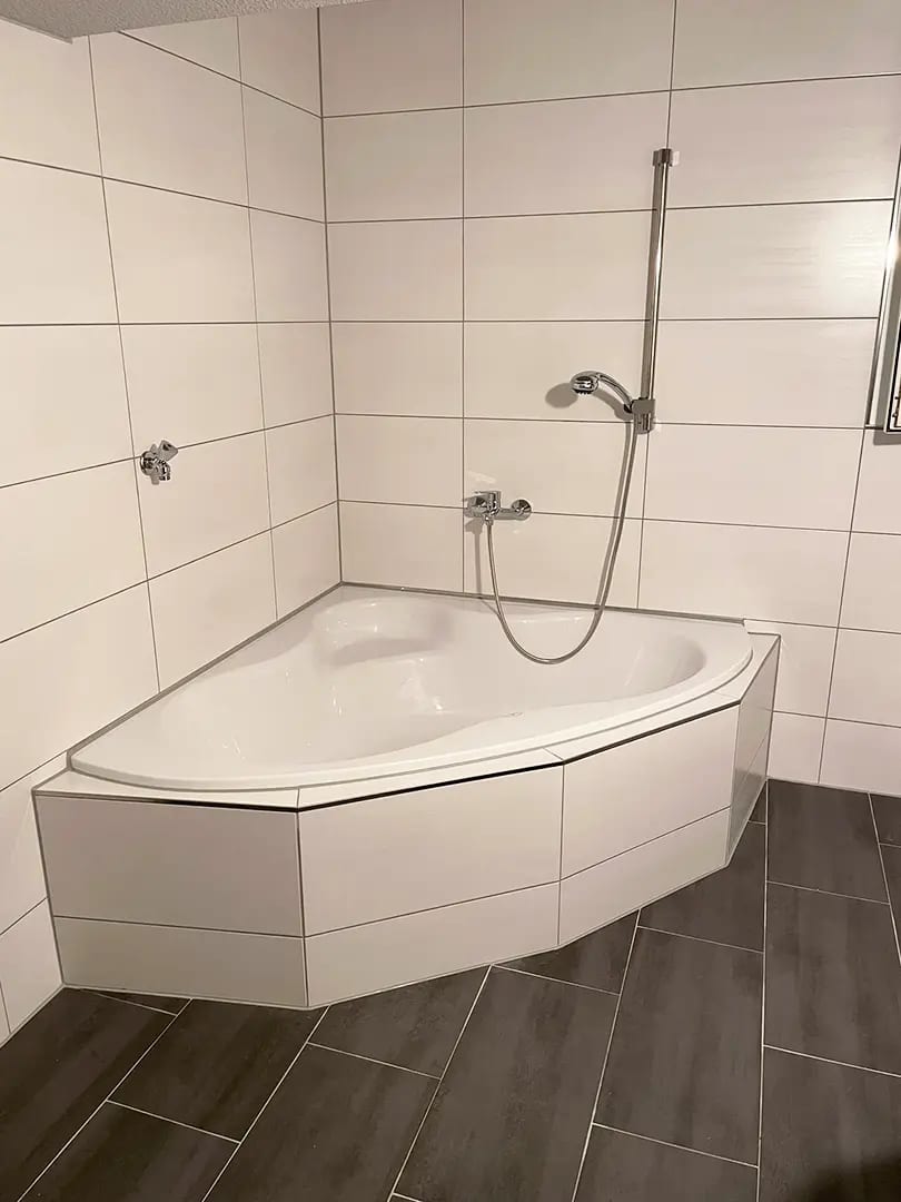 Eckbadewanne mit Duscharmatur vor neu verfliester Wand