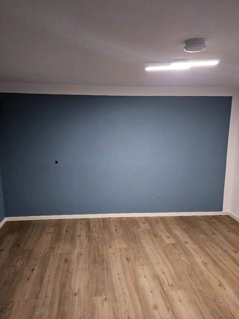 Raum mit blaugrau gestrichener Wandfläche und neuem Bodenbelag in Holzoptik